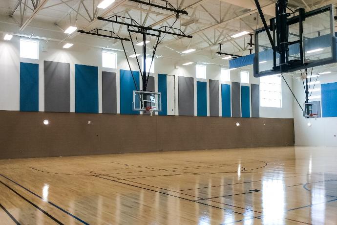 A school basketball gymnasium with Fabricmate wall panel installations around the gym. The panels alternate in height and width and feature grey and dark blue colors.