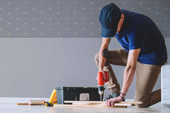 A contractor preparing fabric wall installation pieces on the ground in front of a Fabricmate wall system. The bottom half of the wall is grey and the top portion is a darker shade of grey with a yellow dot pattern.